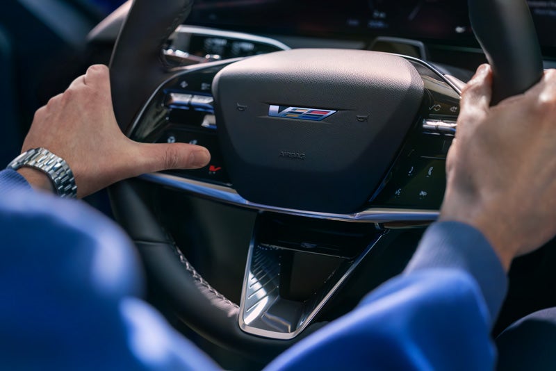 Close-up of a Man About to Press the V-Button on the 2026 OPTIQ-V Steering Wheel | Cadillac of Laguna Niguel in Laguna Niguel CA