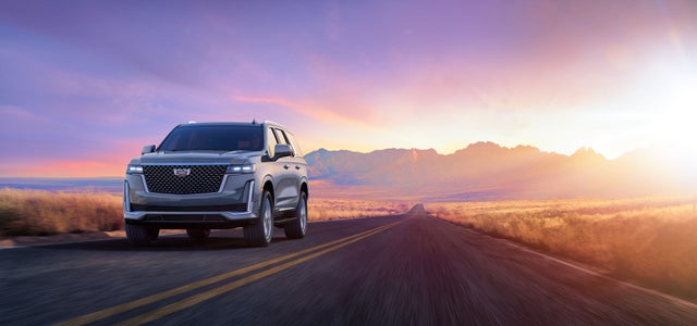 Cadillac Escalade driving on a highway road with mountains in the back during sunset